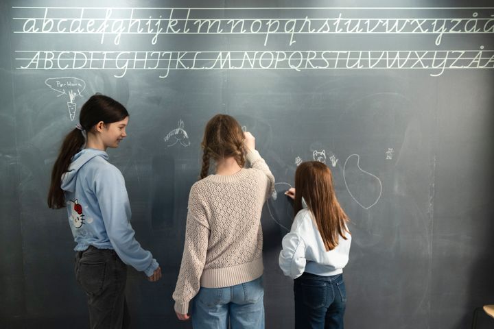 Kolme ihmistä seisoo selin liitutaulun edessä kirjoittamassa.