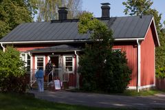 Punainen puutalo kesällä vihreiden puiden ja oksien ympäröimänä.