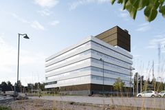 En vit- och brunfärgad byggnad sedd från marknivå. Framför bygganden syns parkerade bilar och en gående person.