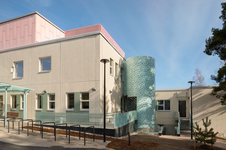 Fasaden på Esbovikens hälsostation i beige, turkosa och ljusröda färgnyanser. I förgrunden syns cykelställ.