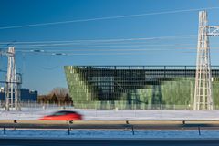 Vihertävä rakennus, jonka edessä sähkölinjoja, etualalla tie ja auto.