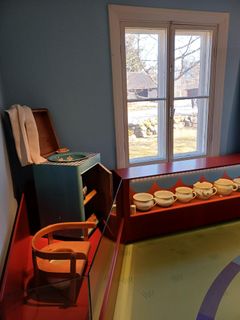 Istuimella varustettu potta, käsienpesuallas sekä posliinipottia hyllyllä esillä.