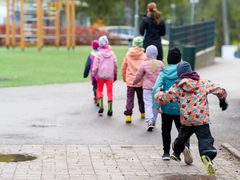 Espoolaisia alakoululaisia koulun pihalla jonossa opettajan takana. Viimeinen oppilas loikkaa iloisesti vesilätäkön yli seuratessaan muita.