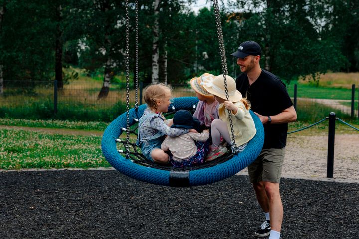 Aikuinen keinuttaa lapsia keinussa asukaspuistossa