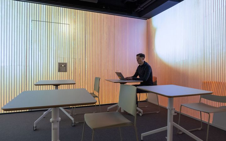 Mies istuu tietokoneen ääressä huoneessa, jossa on virtuaaliset puuseinät.