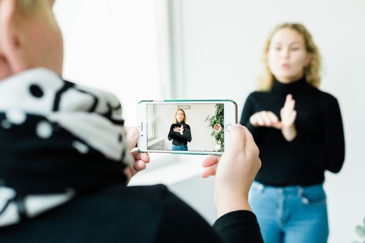 Viittomakielistä puhujaa kuvataan puhelimen kameralla.