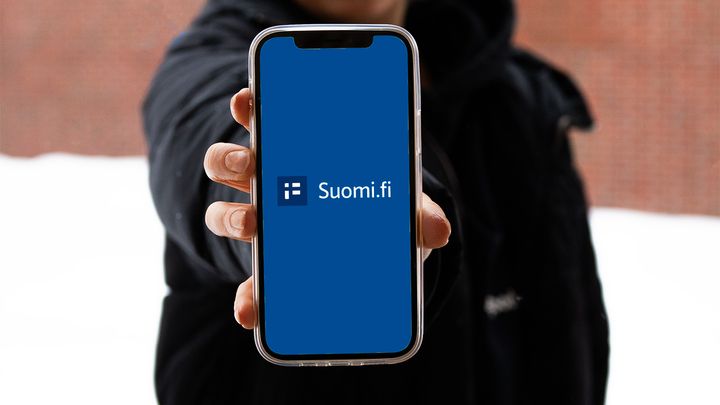 The person shows the phone screen, which shows the Suomi.fi mobile application
