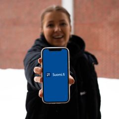 The woman shows the phone screen with the Suomi.fi mobile application.