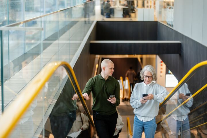Mies ja nainen liukuportaissa älypuhelimet käsissään