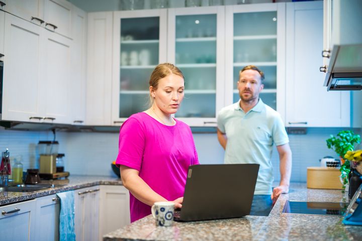 Kuvituskuva. Nainen ja mies keittiössä tietokoneen ääressä.