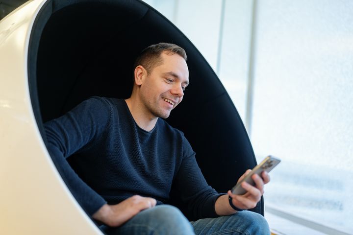 Man sitting in a round chair, smiling while looking at his phone.