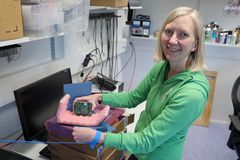 Nainen vihreässä hupparissa pitelee teknistä moduulia laboratoriossa.