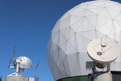 Kaksi satelliittiantennia ja suuri geodeettinen kupoli kirkasta taivasta vasten.