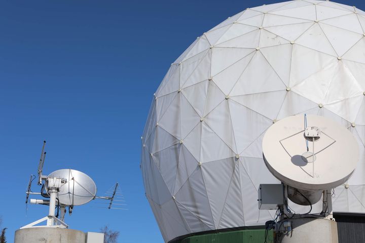 Kaksi satelliittiantennia ja suuri geodeettinen kupoli kirkasta taivasta vasten.