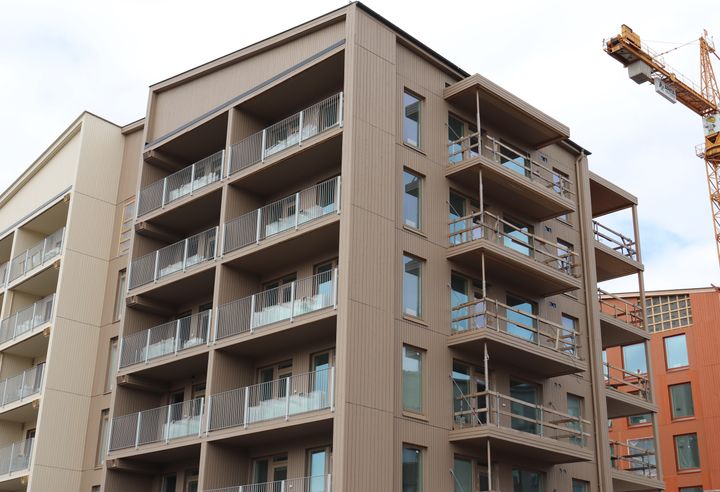 A modern wooden apartment building with several balconies alongside a construction crane.