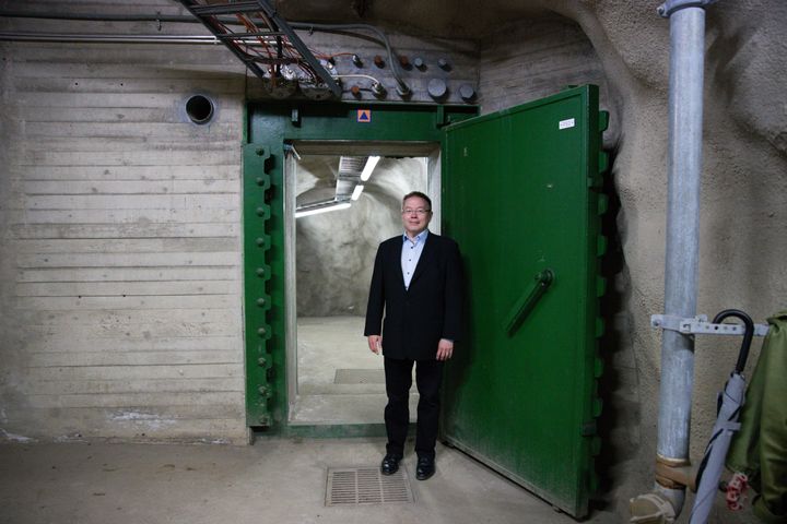 Henkilö seisoo betonisen väestönsuojan sisäänkäynnillä. Taustalla näkyy vihreä ovi ja ilmaputkia.