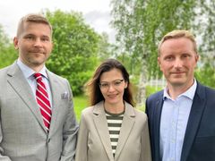 Kolme henkilöä seisoo ulkona vihreässä ympäristössä.