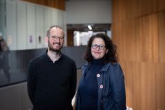 Kaksi henkilöä seisoo vierekkäin sisätilassa, jolla on puiset seinät.