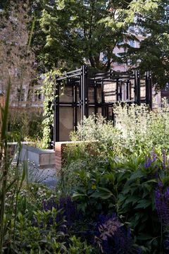 Savesta ja ekologisista materiaaleista rakennettu paviljonki ulkoilmassa, vihreää kasvillisuutta sen ympärillä