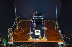 Pieni satelliitti testauslaitteessa, sen ympärillä on johtoja ja antenneja.