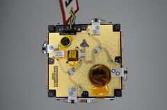 A small satellite with exposed circuit board and wiring on a gray background.