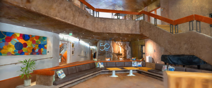 Avara aula, jossa on ruskeat portaat, paljon istumatilaa ja värikäs maalaus seinällä.