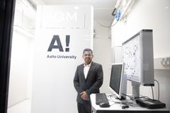 Kuvassa henkilö seisoo tietokoneiden vieressä laboratoriotilassa, jossa on Aalto-yliopiston logo ja teksti "IQM".