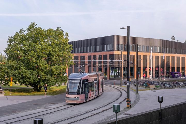 Raitiovaunu liikkuu Otaniemen kampuksella tiilirakennuksen edustalla.