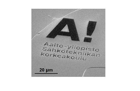 Elektronimikroskooppikuva: Aalto-yliopiston logo atomisen ohuella materiaalilla, jonka alla teksti "Sähkötekniikan korkeakoulu". Mittakaava 20 mikrometriä.