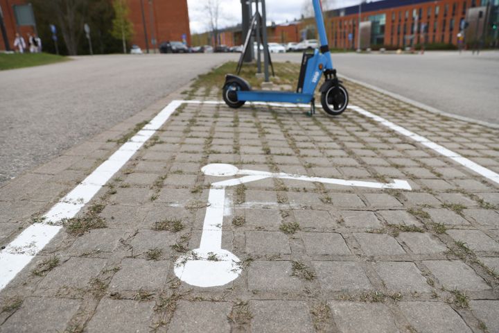 Kuvassa maahan piirretty valkoisella rajat sekä potkulautaa esittävä kuva. Rajojen sisällä on yksi potkulauta parkattuna.