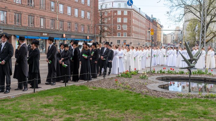 Joukko ihmisiä juhlapuvuissa katualueella promootiokulkueessa keväällä.