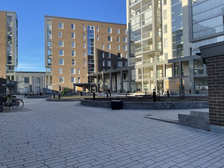 Moderni kerrostaloalue, jossa on sisäpiha, penkkejä ja polkupyöriä telineessä.