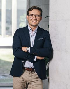 Aleksi Niittymies seisoo hymyillen puku päällä kädet ristissä.