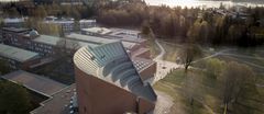 Ilmakuva Aalto-yliopiston kampusalueesta, jossa näkyy aaltomainen kattorakenne, kampusrakennuksia ja puustoista ympäristöä.