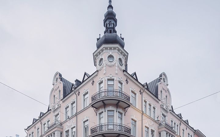 Vaaleanpunainen koristeellinen kulmatalo, jossa on ranskalaiset parvekkeet ja torni.