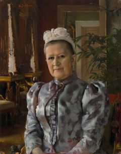 En person sitter på en stol och det finns en stor grön växt i bakgrunden.