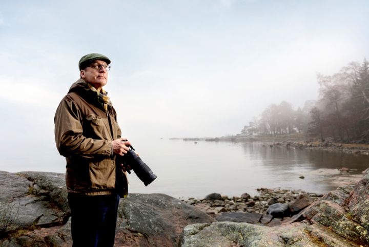 Mies kameroineen tunnelmallisessa merimaisemassa luontokuvaajan varusteissa.