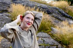 Nuori nainen kallioisella kumpareella, sitoo molemmin käsin hiuksiaan ja katsoo kirkkain silmin kohti avaraa luontoa.