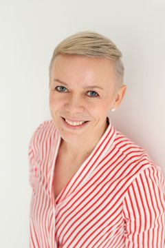 Raitapaitainen nainen hymyilee.