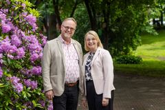 Mies ja nainen katsovat hymyillen kameraan. Taustalla kukkivia alppiruusuja.