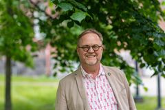 Vaaleaan puvuntakkiin pukeutunut silmälasipäinen mies katsoo hymyillen kameraan.