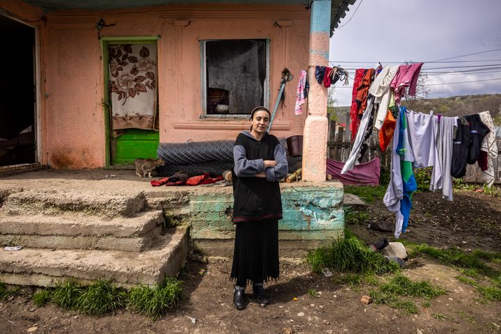 Nainen seisoo kädet rinnalle ristittynä talon edessä. Taustalla pyykkinaru ja pyykkiä.