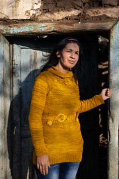 Keltaiseen paitaan pukeutunut tummahiuksinen nainen nojaa ovenkarmiin.