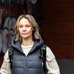 Kuvassa on ulkovaatteisiin pukeutunut nainen, joka katsoo suoraan kameraan vakava ilme kasvoillaan.