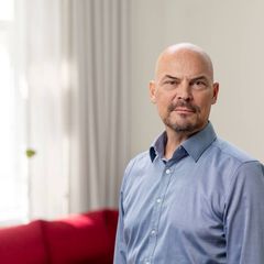 Kuvassa on vaaleansiniseen kauluspaitaan pukeutunut mies, joka katsoo suoraan kameraan vakava ilme kasvoillaan.