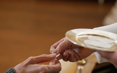 Käsi ojentaa ehtoollisleipää alttarilla ehtoollisen nauttijalle.