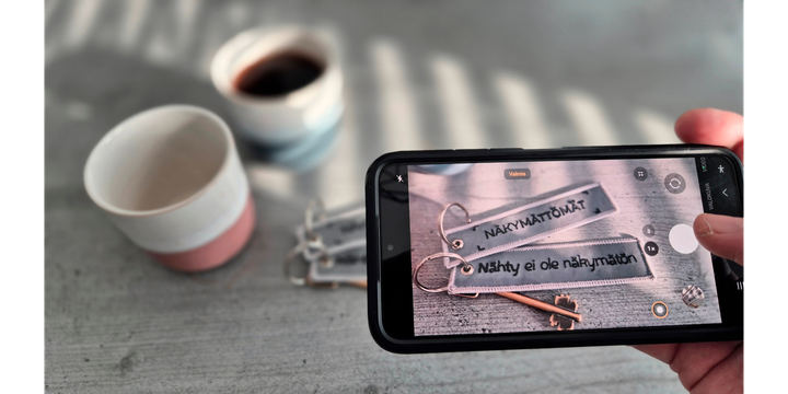 Kahvikuppi ja Näkymättömät-avaimenperä pöydällä.