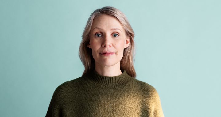 Henkilö vihreässä villapaidassa vaalean taustaa vasten.