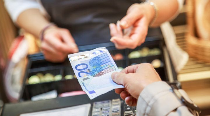Henkilö ojentaa 20 euron setelin kassalla myyjälle.
