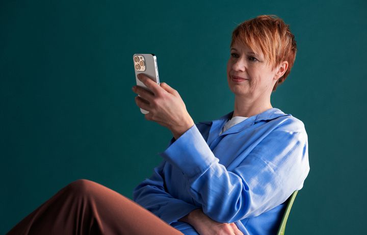 Henkilö katsoo älypuhelintaan sinisessä kauluspaidassa.